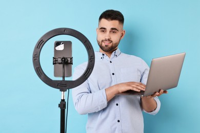 Technology blogger reviewing laptop and recording video with smartphone and ring lamp on light blue background