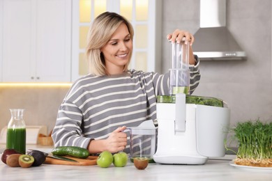 Photo of Smiling woman with fresh products using juicer at white marble table in kitchen