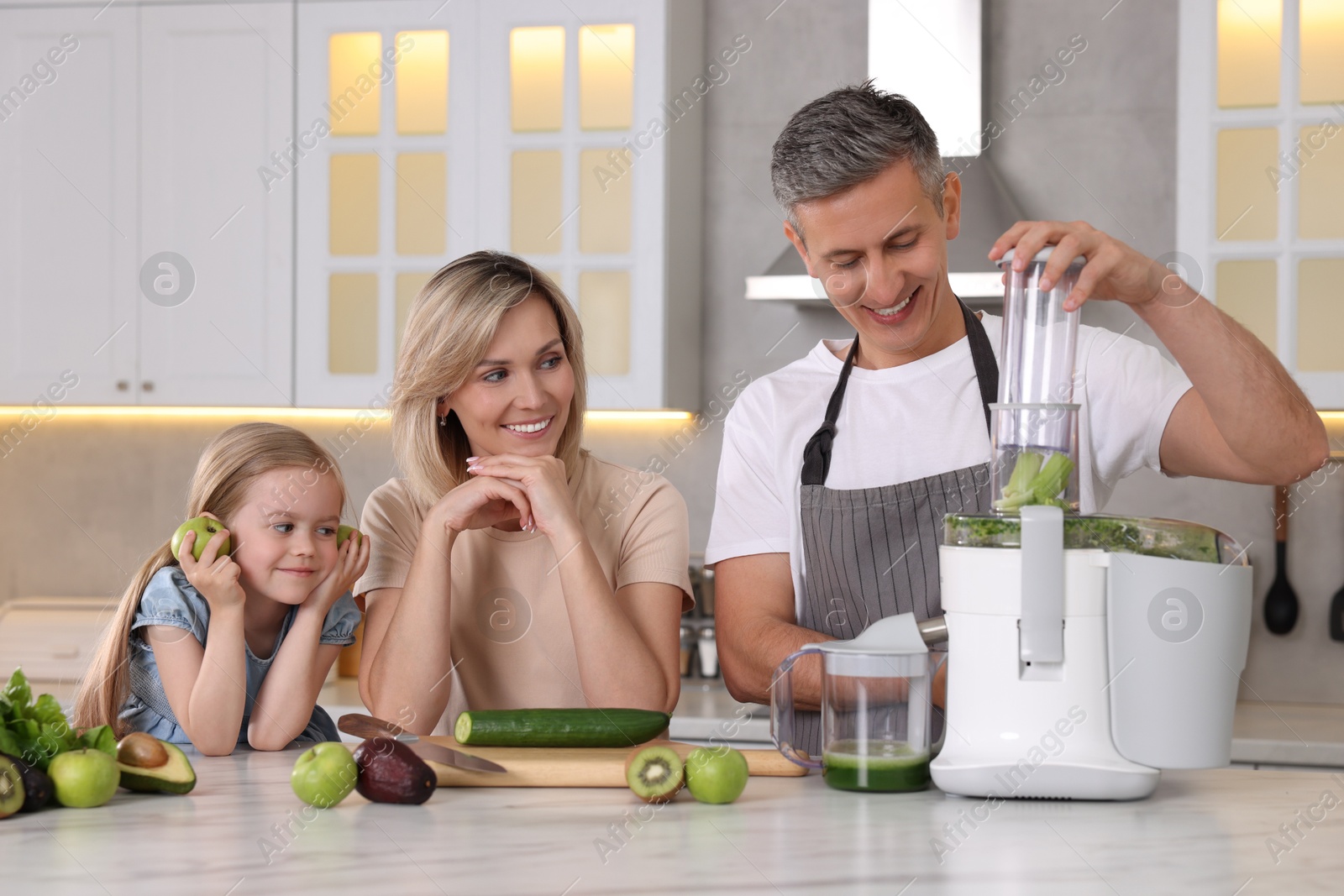 Photo of Happy family with juicer and fresh products making drink at white marble table in kitchen