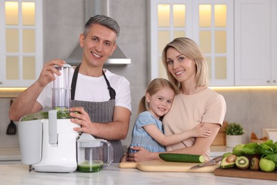 Photo of Happy family with juicer and fresh products making drink at white marble table in kitchen