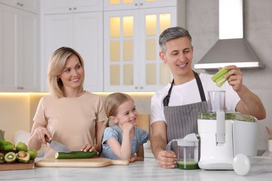 Photo of Happy family with juicer and fresh products making drink at white marble table in kitchen