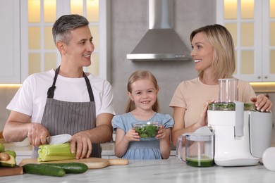 Photo of Happy family with juicer and fresh products making drink at white marble table in kitchen