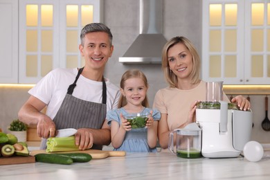 Happy family with juicer and fresh products making drink at white marble table in kitchen