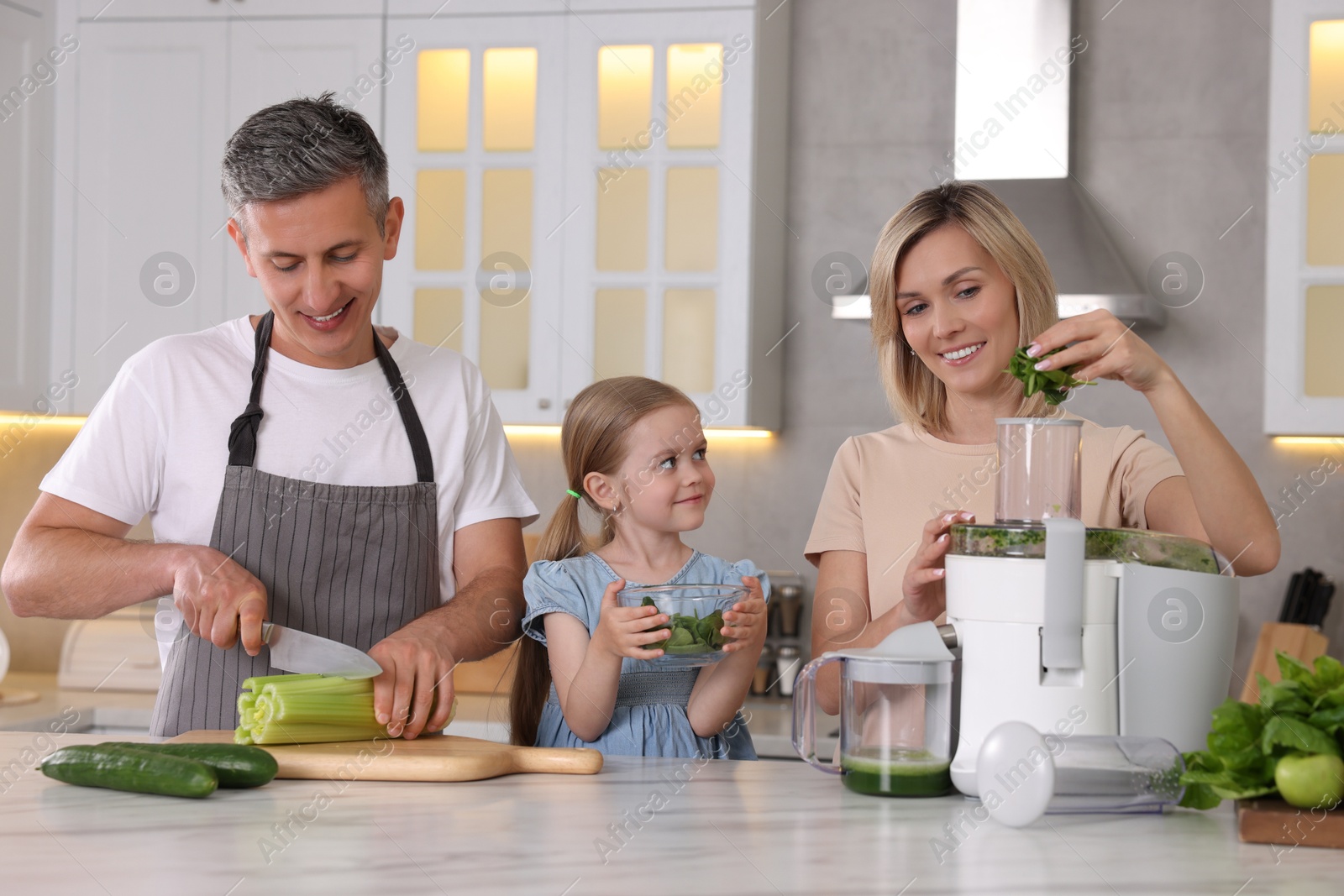 Photo of Happy family with juicer and fresh products making drink at white marble table in kitchen