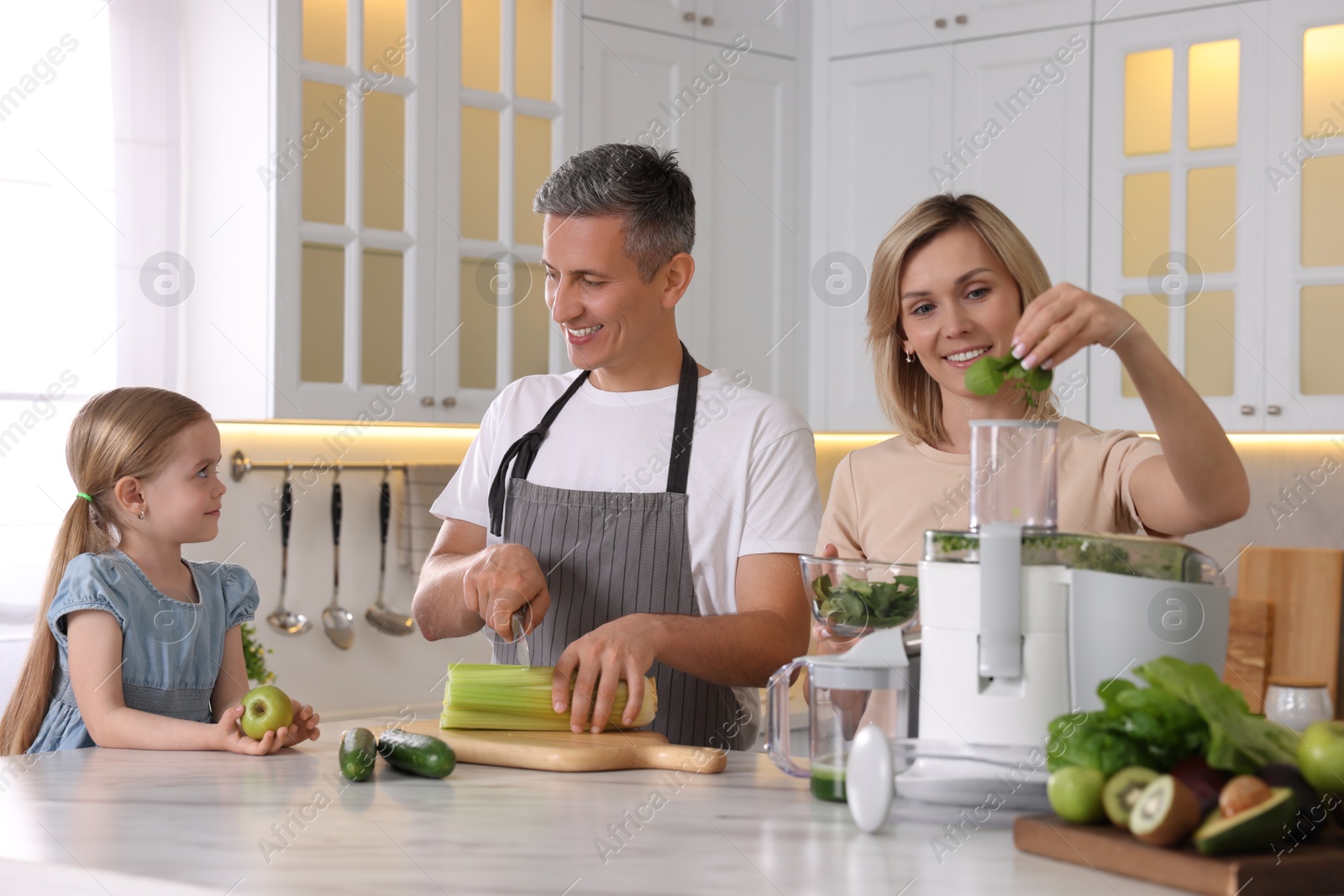 Photo of Happy family with juicer and fresh products making drink at white marble table in kitchen