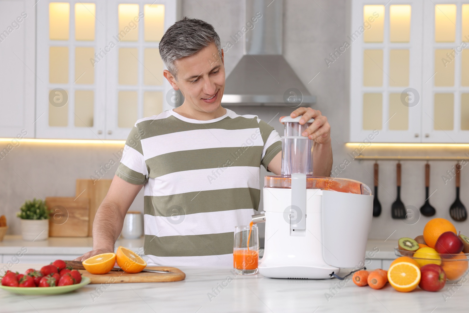 Photo of Man with fresh products using juicer at white marble table in kitchen