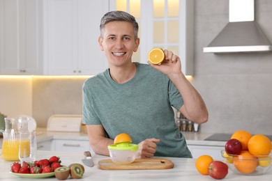 Photo of Making juice. Smiling man with orange at white marble table in kitchen