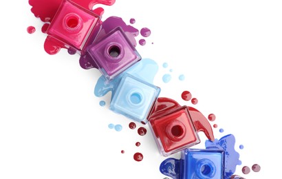 Many bottles and drops of colorful nail polishes isolated on white, top view