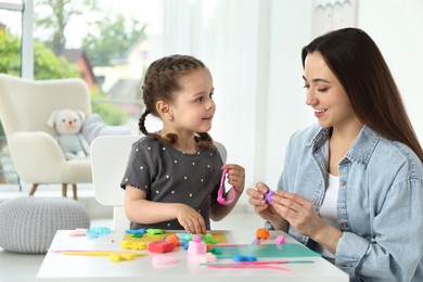 Photo of Smiling mother and her daughter sculpting with play dough at table indoors