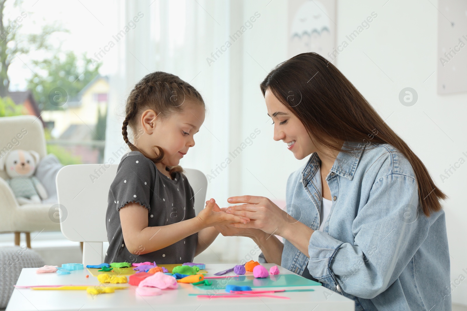 Photo of Smiling mother and her daughter sculpting with play dough at table indoors