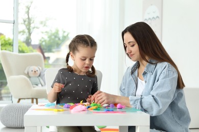 Mother and her daughter sculpting with play dough at table indoors