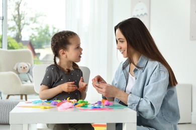 Photo of Smiling mother and her daughter sculpting with play dough at table indoors