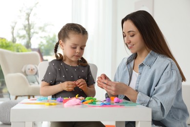 Smiling mother and her daughter sculpting with play dough at table indoors