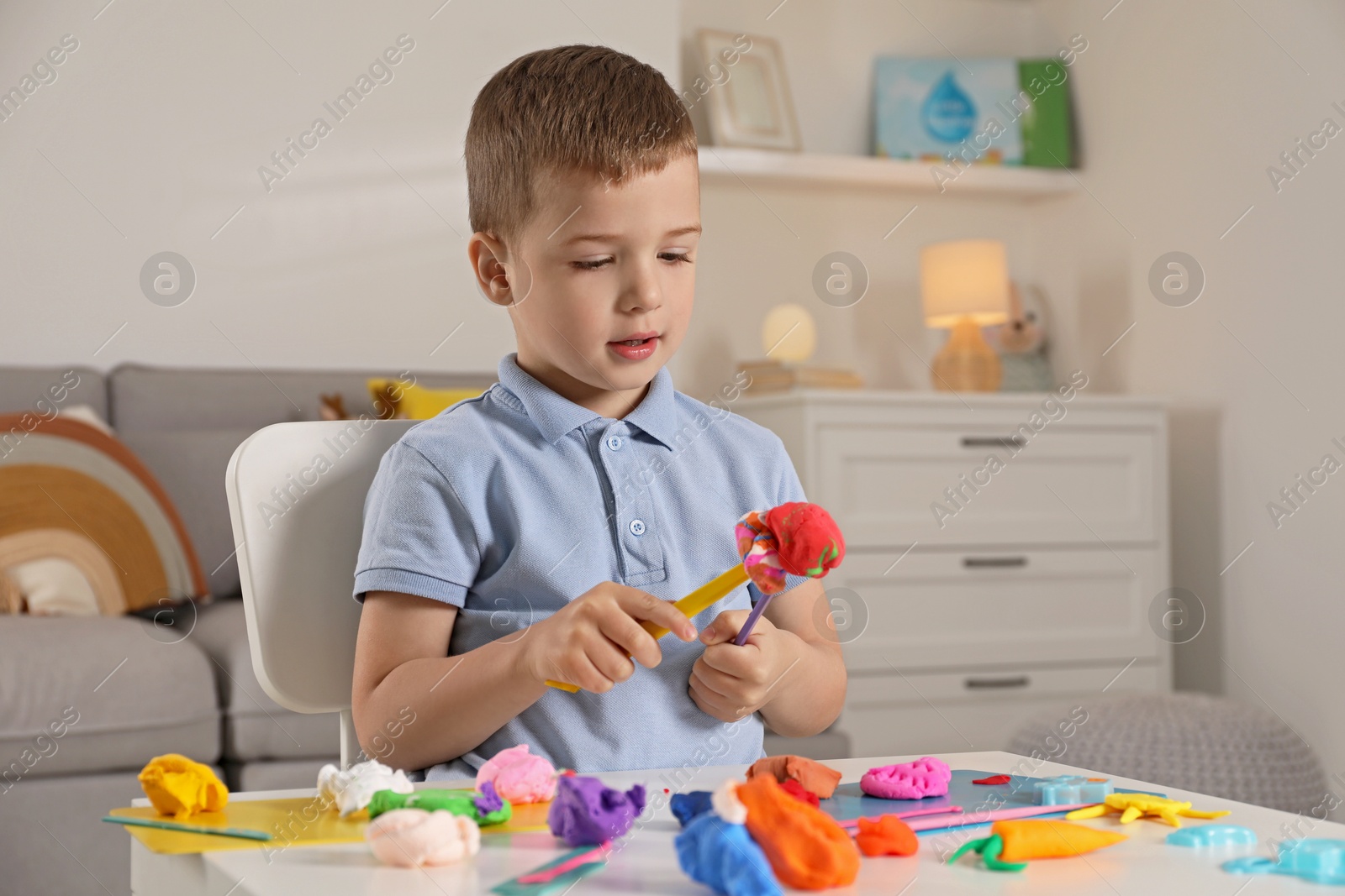 Photo of Little boy sculpting with play dough at table indoors