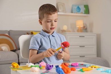 Little boy sculpting with play dough at table indoors