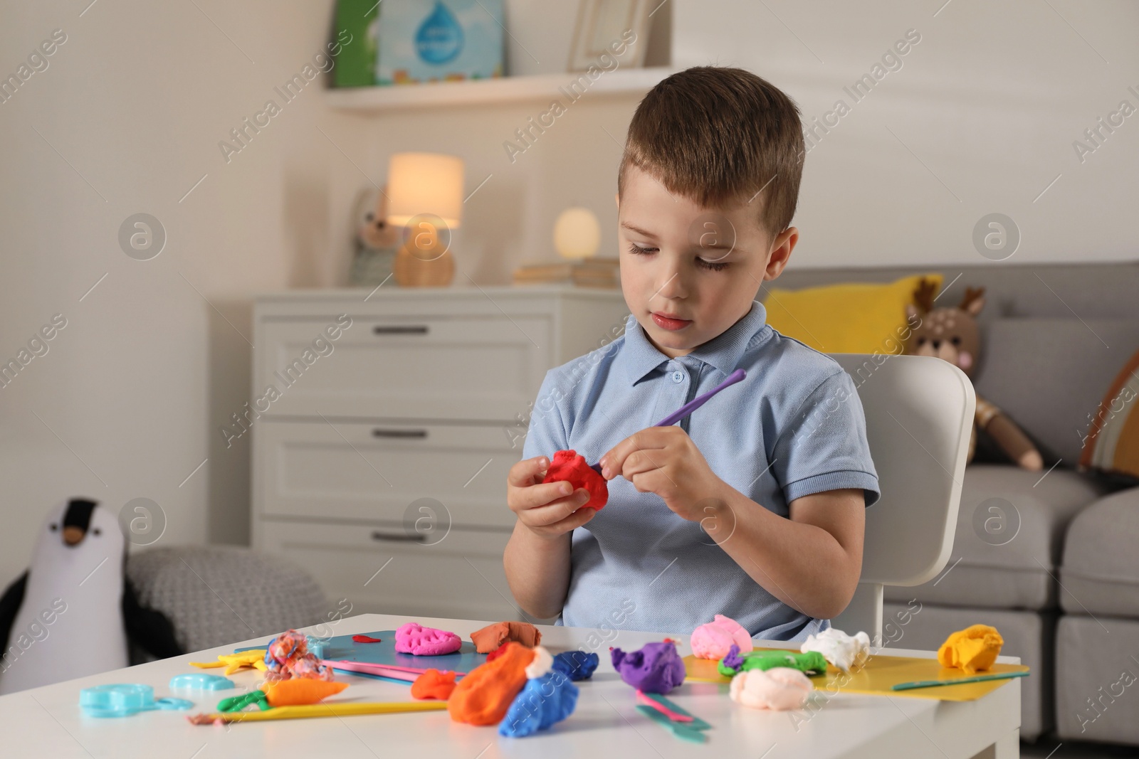 Photo of Little boy sculpting with play dough at table indoors