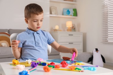 Photo of Little boy sculpting with play dough at table indoors