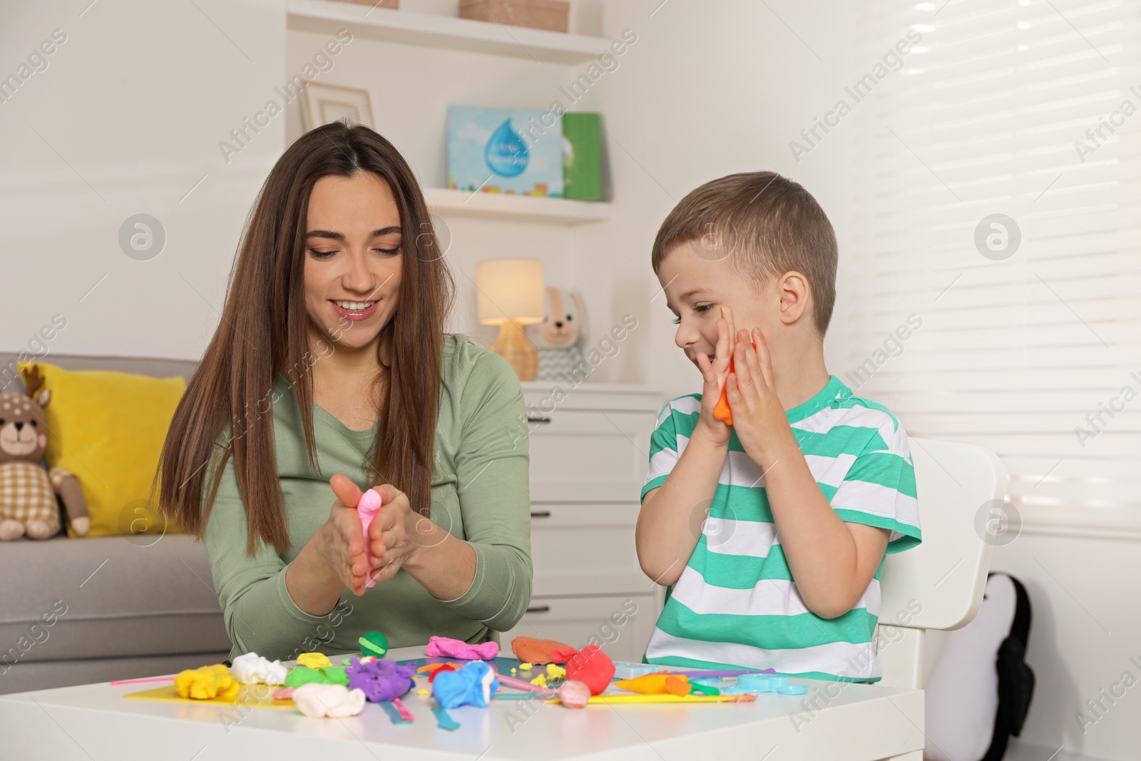 Photo of Smiling mother and her son sculpting with play dough at table indoors