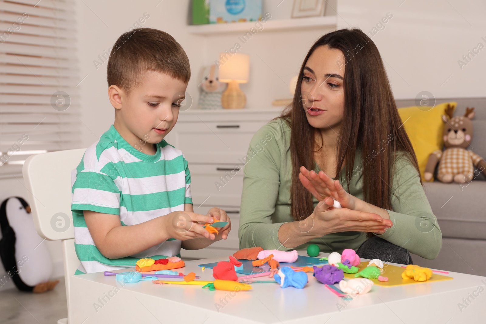 Photo of Son and mother sculpting with play dough at table indoors