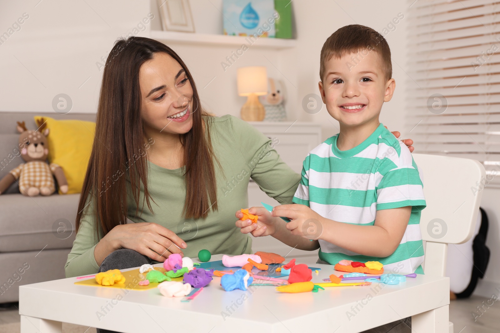 Photo of Smiling mother and her son sculpting with play dough at table indoors