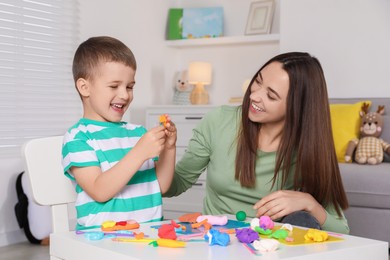 Photo of Smiling mother and her son sculpting with play dough at table indoors