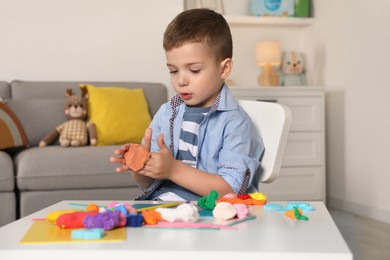 Little boy sculpting with play dough at table in kindergarten