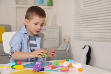 Little boy sculpting with play dough at table in kindergarten. Space for text