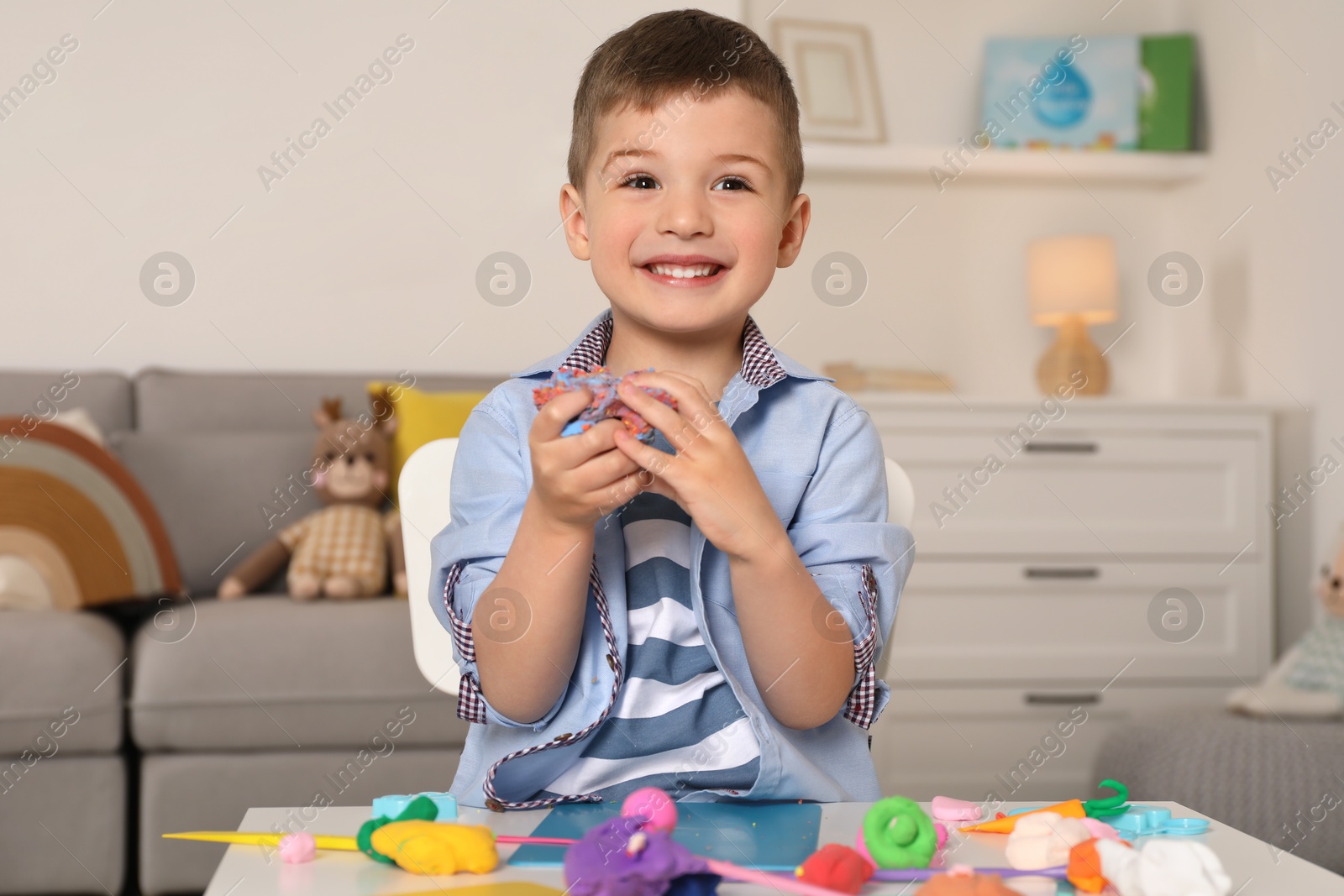 Photo of Smiling boy sculpting with play dough at table in kindergarten