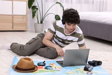 Photo of Travel blogger in headphones using laptop for planning trip at home