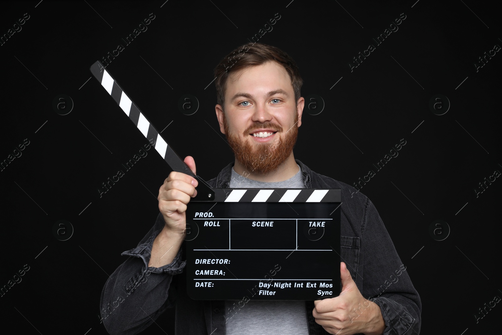 Photo of Making movie. Smiling man with clapperboard on black background