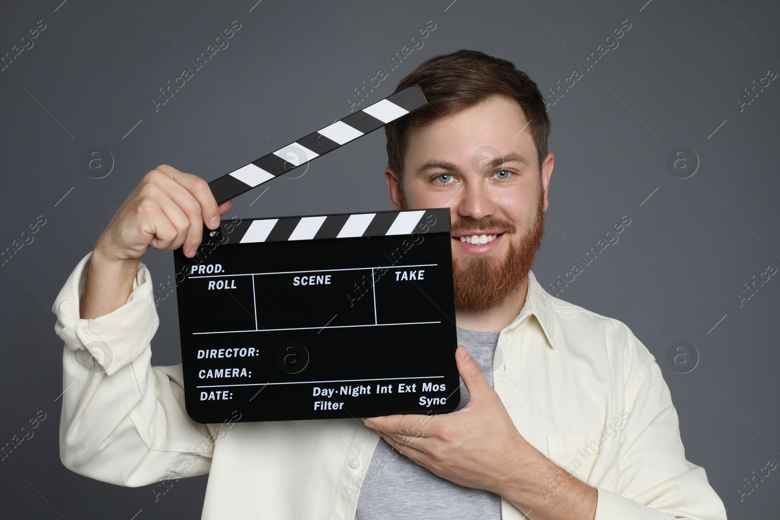 Photo of Making movie. Smiling man with clapperboard on grey background