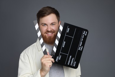 Photo of Making movie. Smiling man with clapperboard on grey background