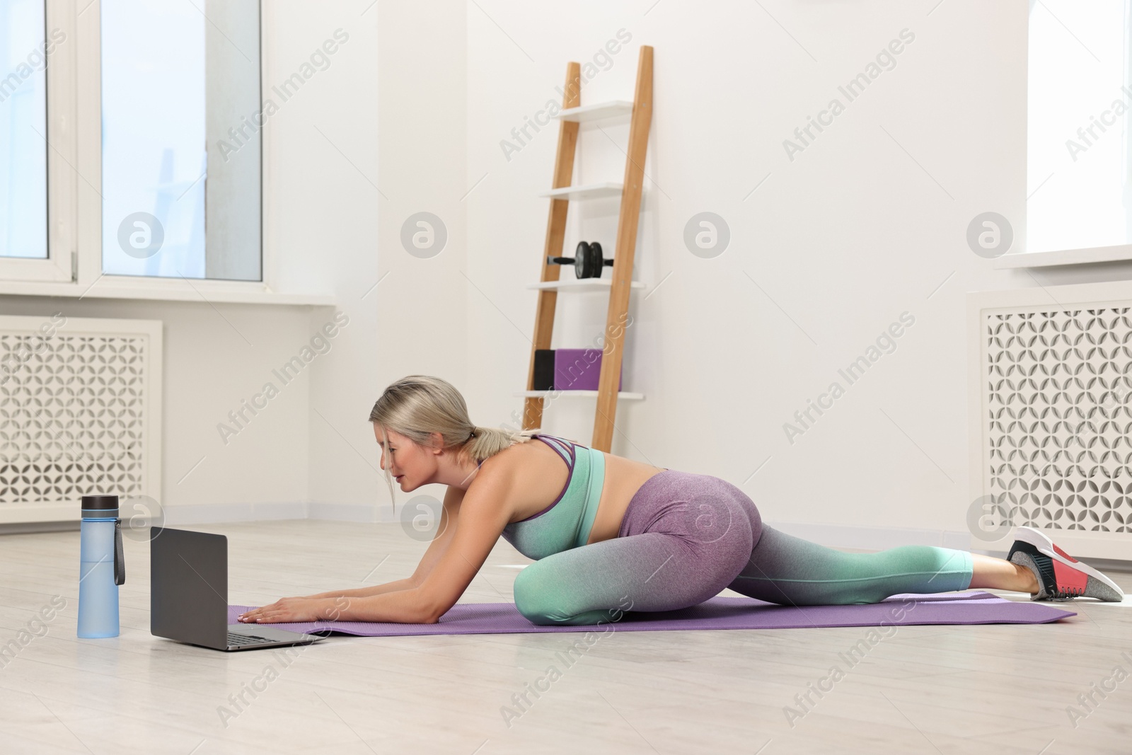 Photo of Online fitness trainer. Woman doing exercise near laptop at home
