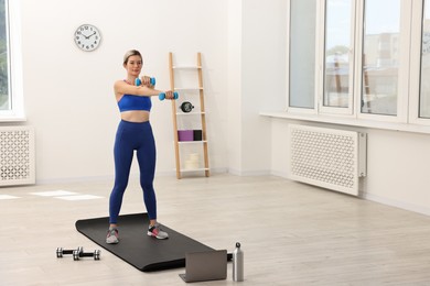 Photo of Online fitness trainer. Woman doing exercise with dumbbells near laptop at home