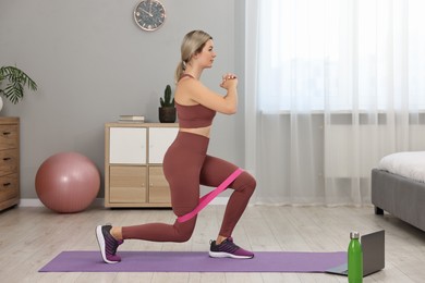 Photo of Online fitness trainer. Woman doing exercise with elastic band near laptop at home