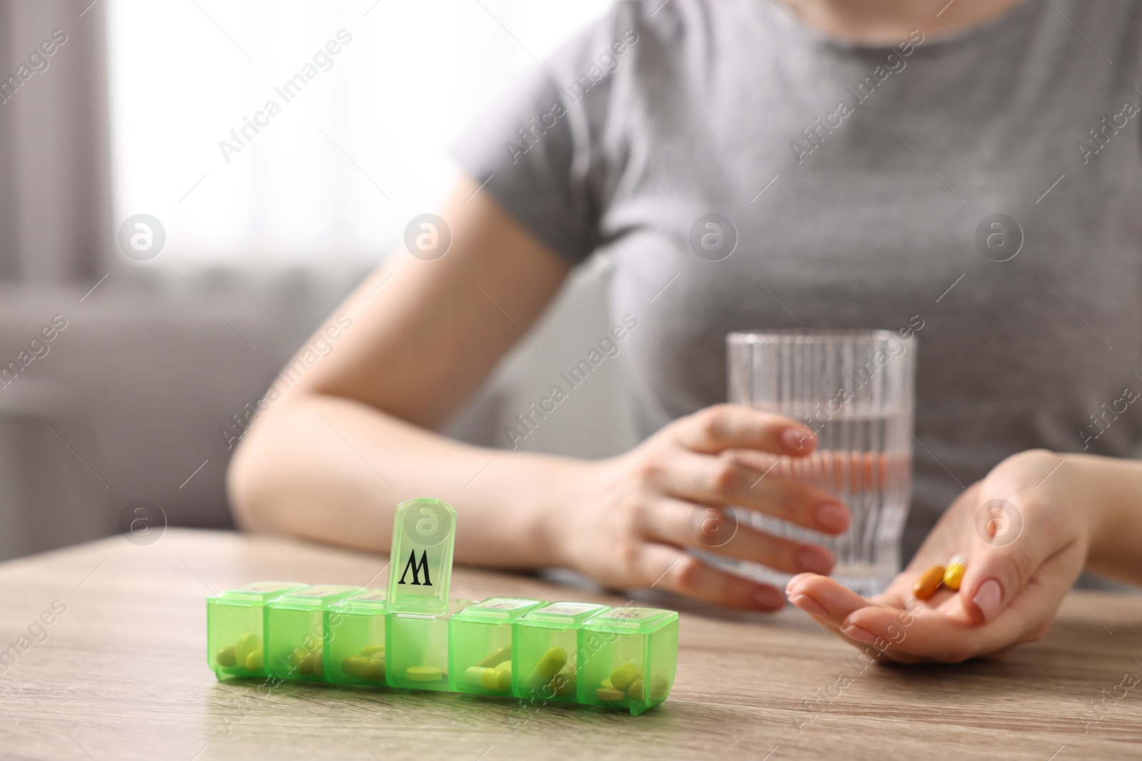 Photo of Woman with pills, organizer and glass of water at wooden table, closeup