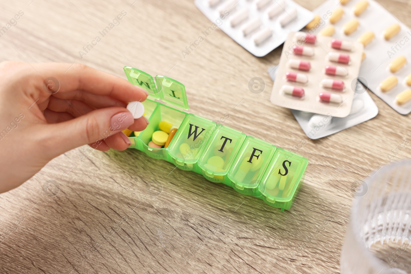 Photo of Woman with pills, organizer and glass of water at wooden table, closeup