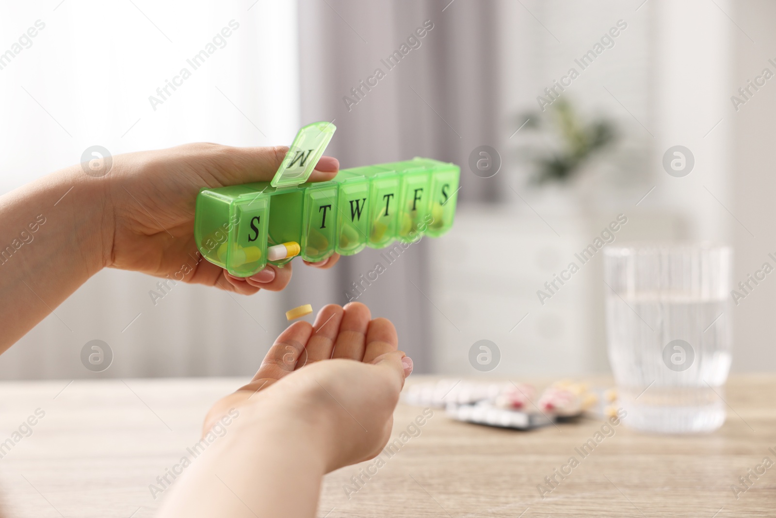 Photo of Woman with pills, organizer and glass of water at wooden table, closeup