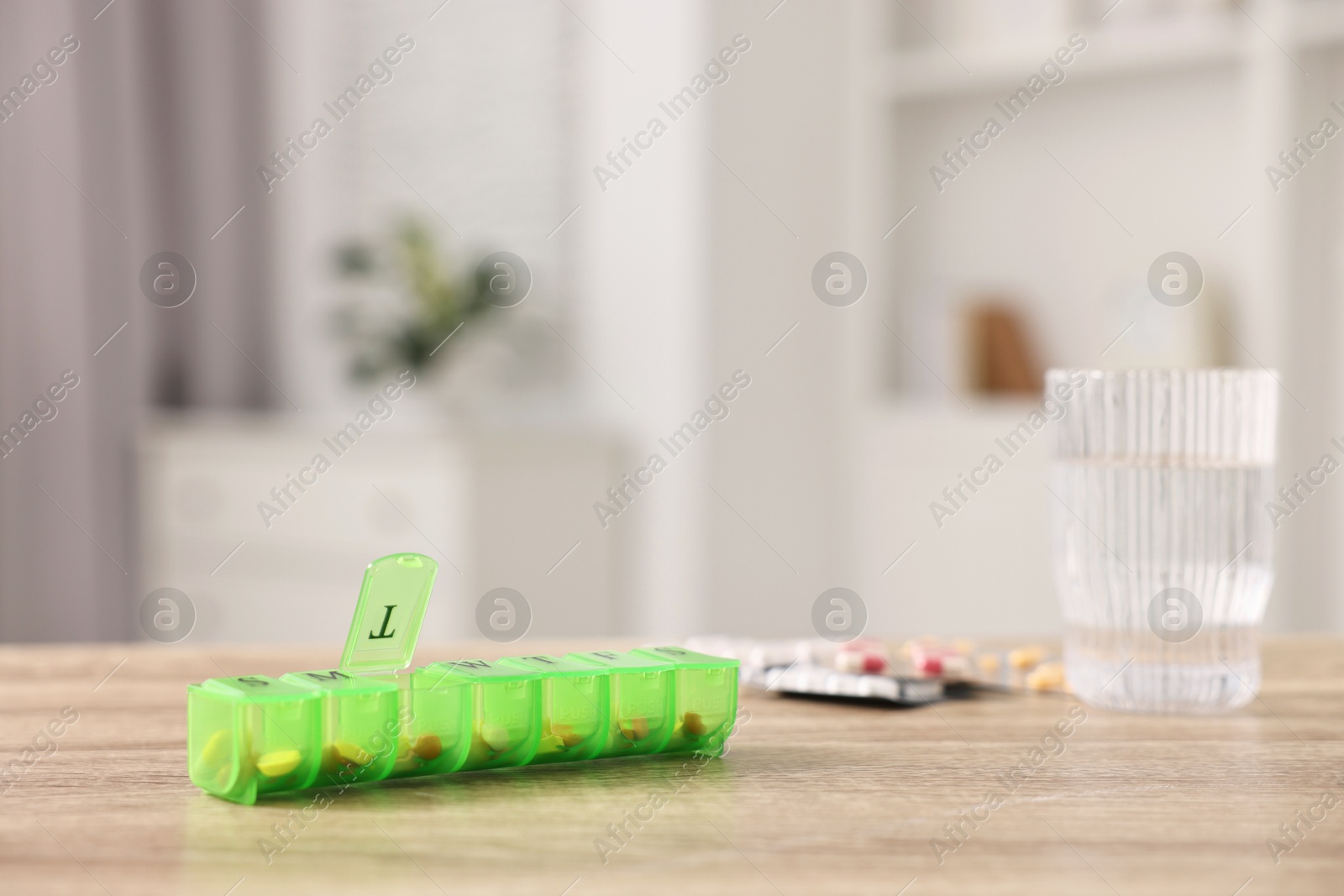 Photo of Different pills, organizer and glass of water at wooden table, closeup. Space for text