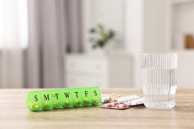 Different pills, organizer and glass of water at wooden table, closeup. Space for text