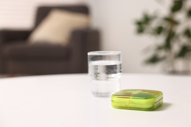 Different pills in organizer and glass of water at white table, closeup. Space for text