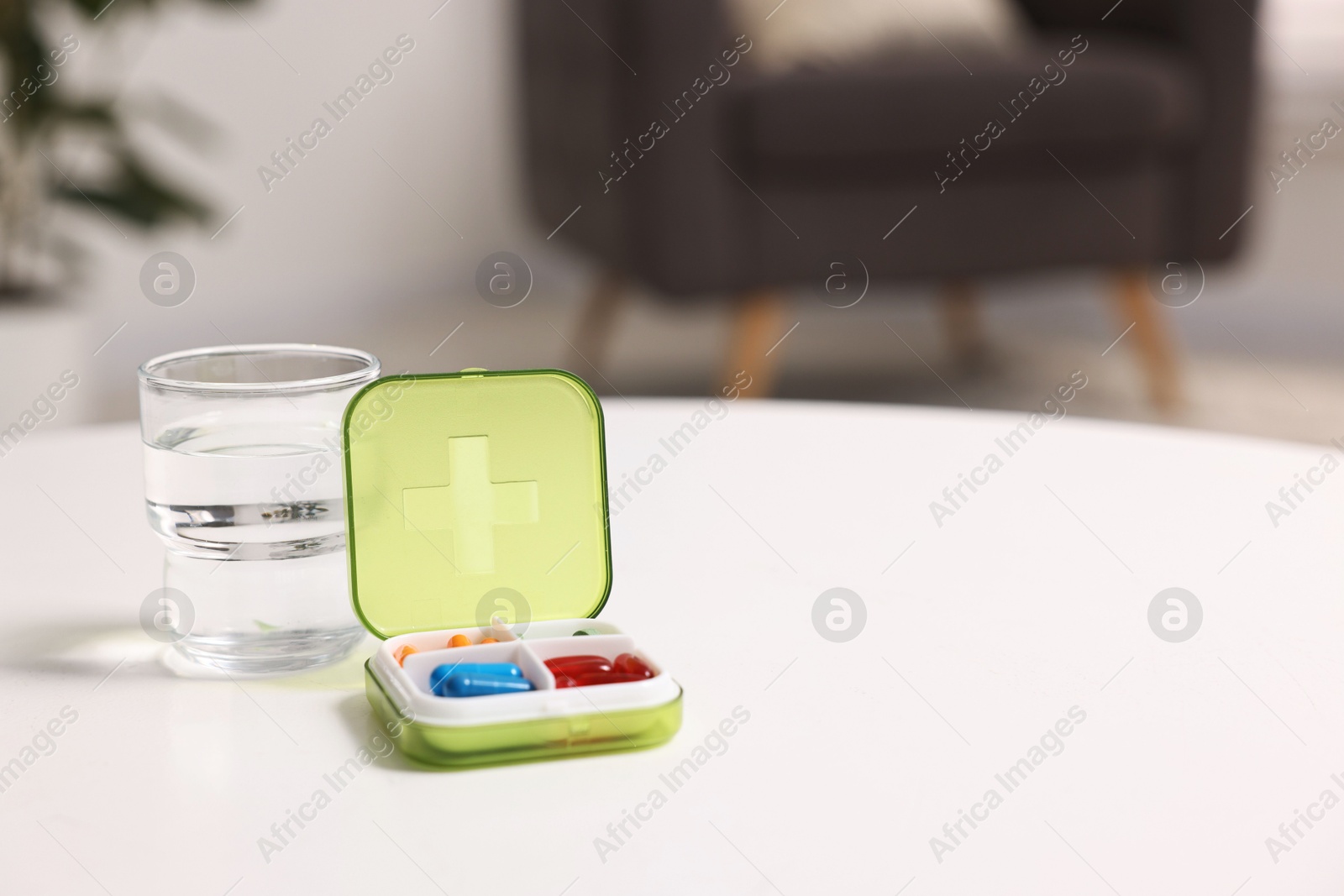 Photo of Different pills in organizer and glass of water at white table, closeup. Space for text