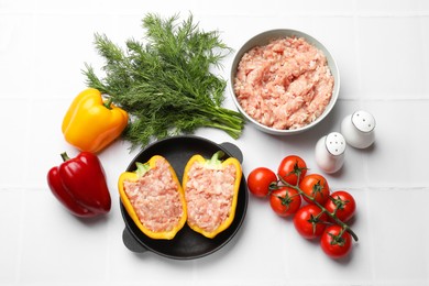 Raw stuffed peppers with ground meat and ingredients on white tiled table, flat lay