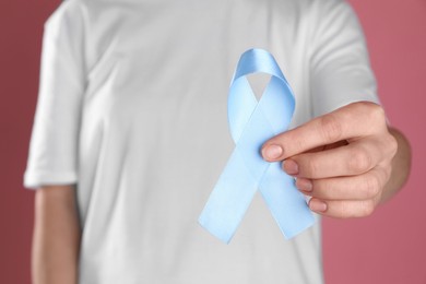 International Psoriasis Day. Woman with light blue ribbon as symbol of support on pink background, closeup