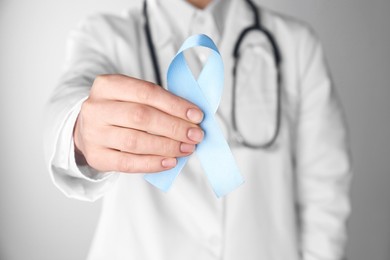 Photo of International Psoriasis Day. Doctor with light blue ribbon as symbol of support on white background, closeup