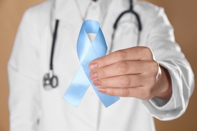 Photo of International Psoriasis Day. Doctor with light blue ribbon as symbol of support on beige background, closeup
