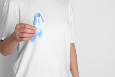 Photo of International Psoriasis Day. Woman with light blue ribbon as symbol of support on white background, closeup. Space for text