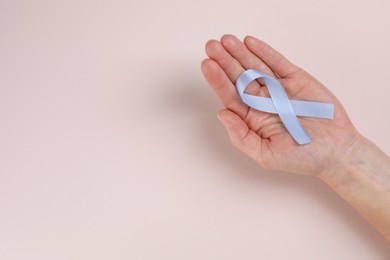 Photo of International Psoriasis Day. Woman with light blue ribbon as symbol of support on beige background, top view. Space for text