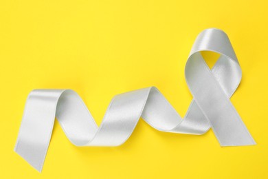 Photo of International Psoriasis Day. Ribbon as symbol of support on yellow background, top view