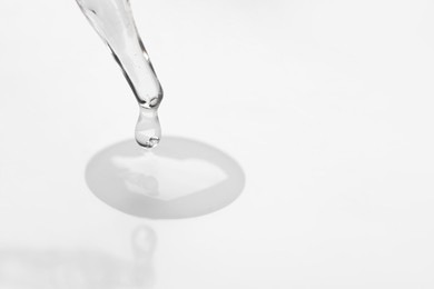 Glass pipette and transparent liquid on white background, closeup. Space for text
